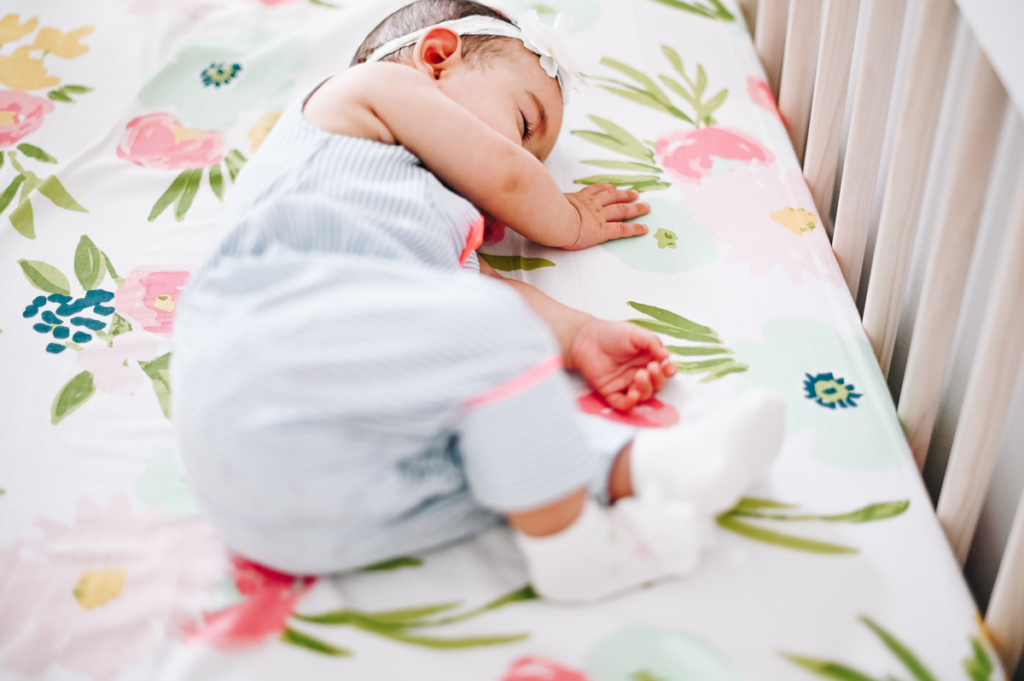 An image of a baby asleep on her side in a crib.