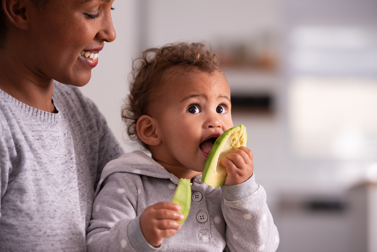 An infant licks a piece of avocado and smiles.