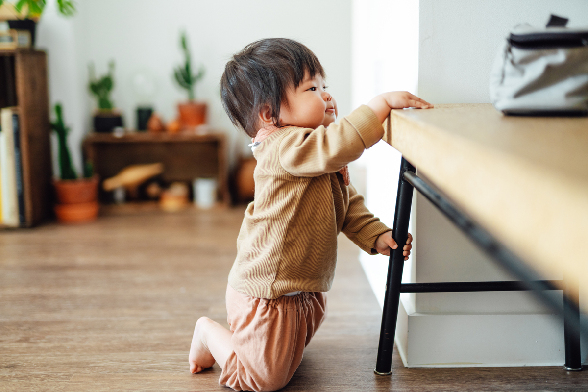 A baby pulls themself up to stand at a bench.