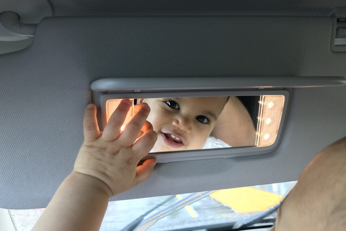 A baby smiles into the review mirror of a car.