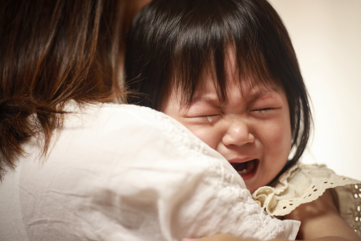 A baby cries on their parent's shoulder during daycare drop-off.