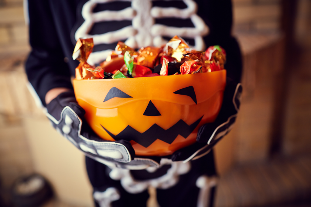 A kid in a skeleton costume holding a pumpkin-shaped bowl of candy.