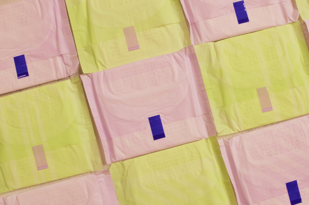 Yellow and pink menstrual pads are arranged in a checkerboard pattern.