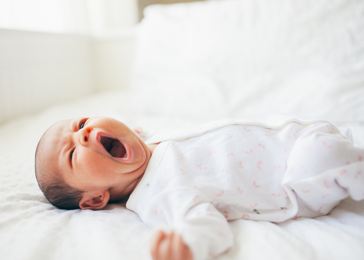 Baby yawns while on their back in a crib.