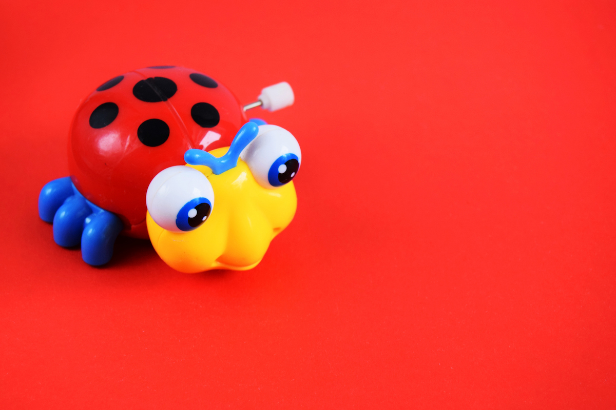 A plastic wind-up lady bug baby toy is seen on a red background