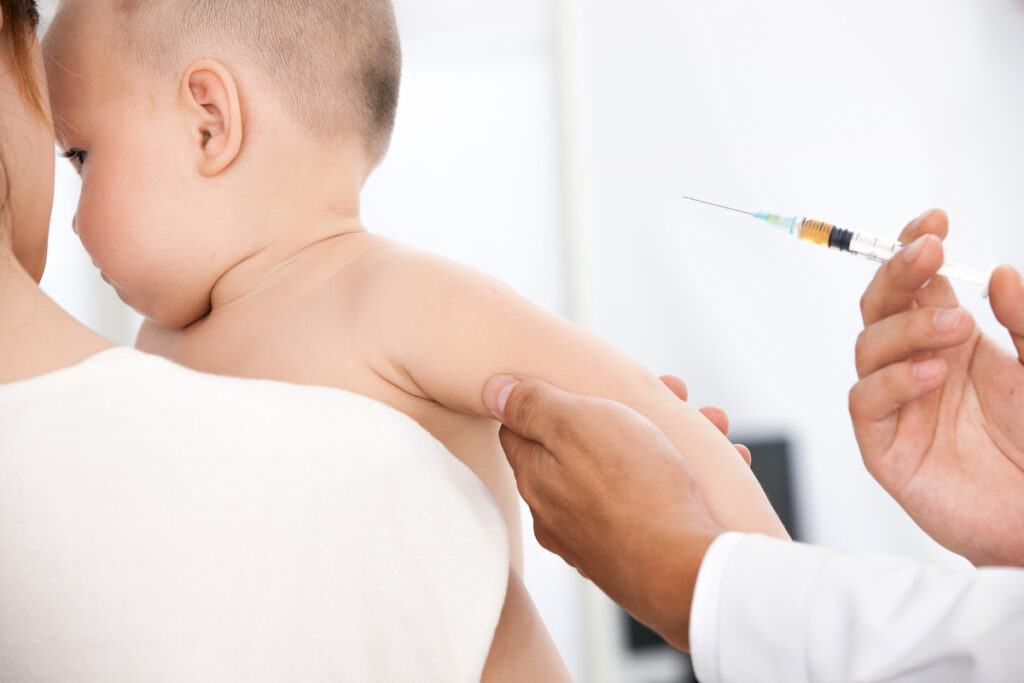 A parent holds a baby while a doctor administers a vaccine.