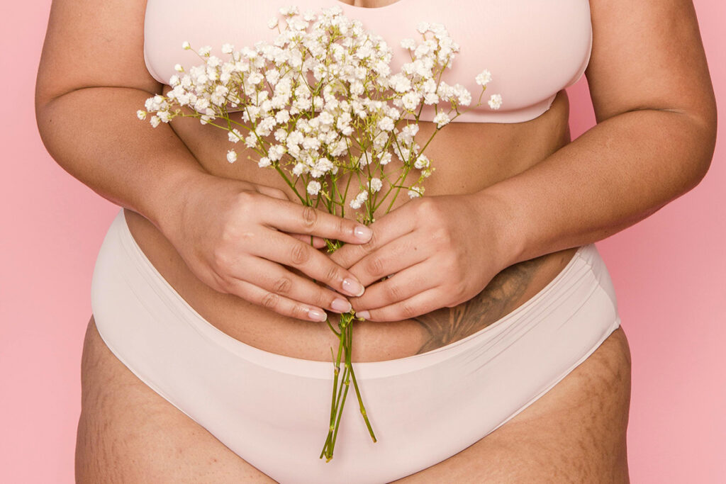 Woman in beige underwear and bra set holding a bouquet of flowers.