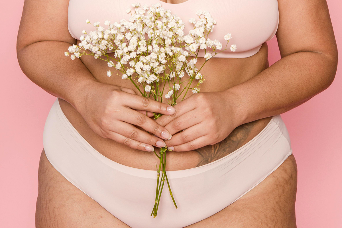 Woman in beige underwear and bra set holding a bouquet of flowers.