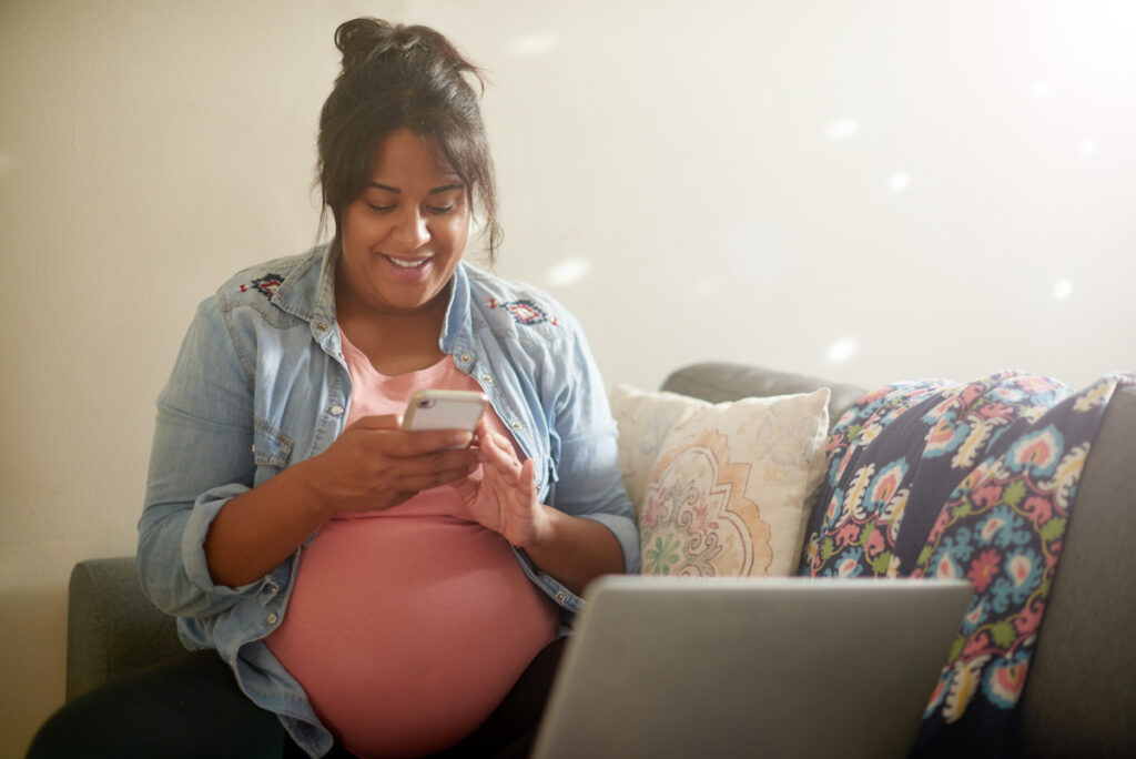 Pregnant woman reads her phone while sitting on a couch