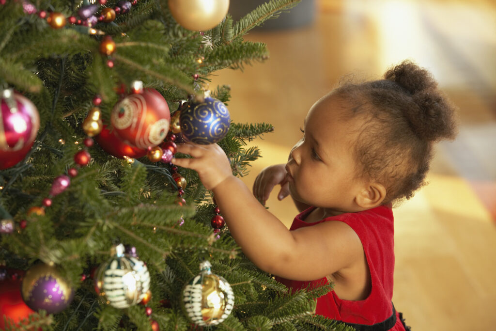 A toddler grabs and stands by a christmas tree