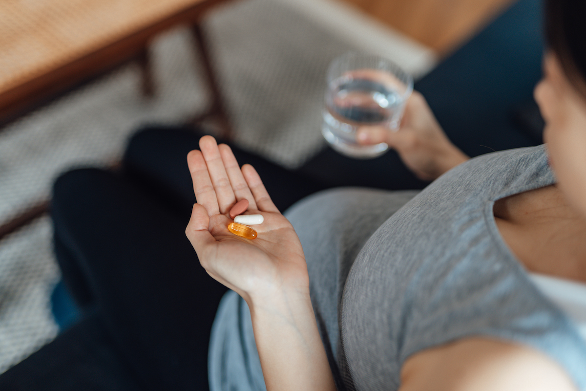 Pregnant woman holds vitamins and a glass of water