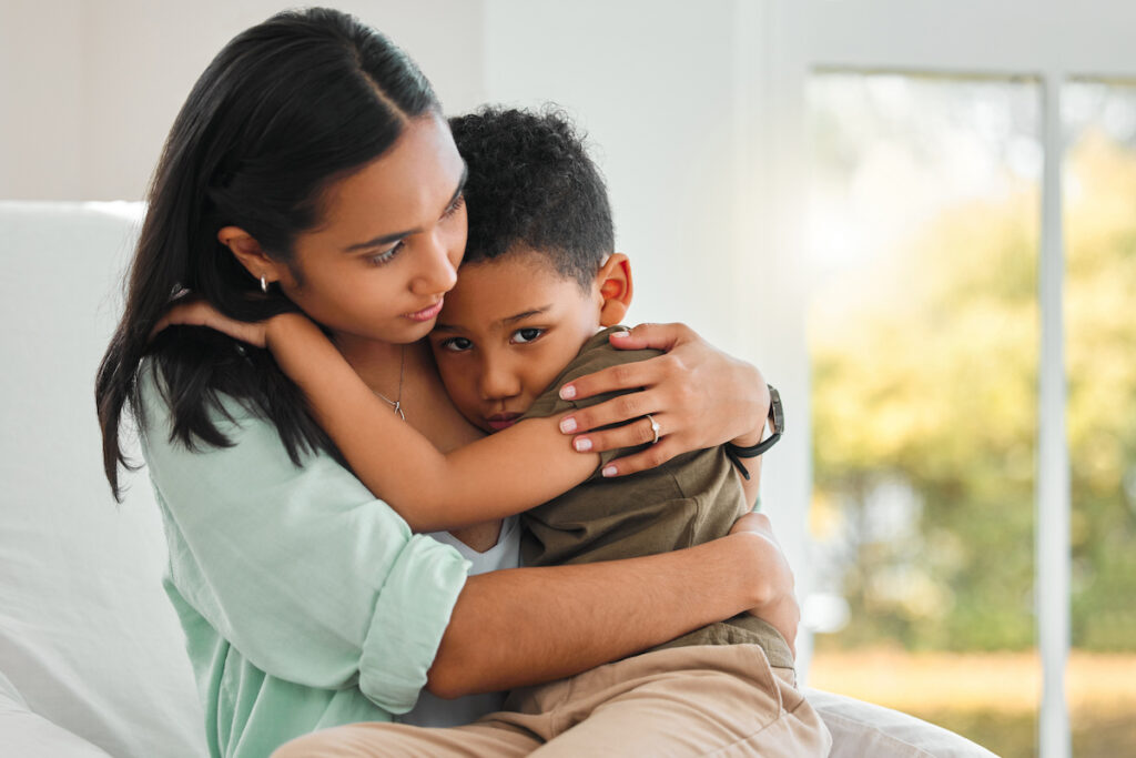 A parent holds a young child. Both look sad.