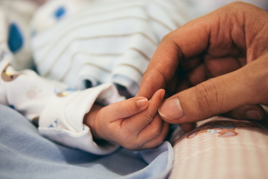 A new parent holds the fingers of their baby after birth.