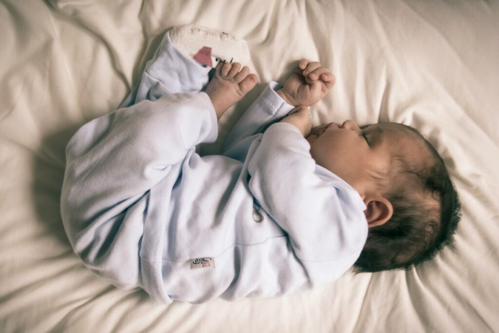 A sleeping baby is curled up on a white sheet.