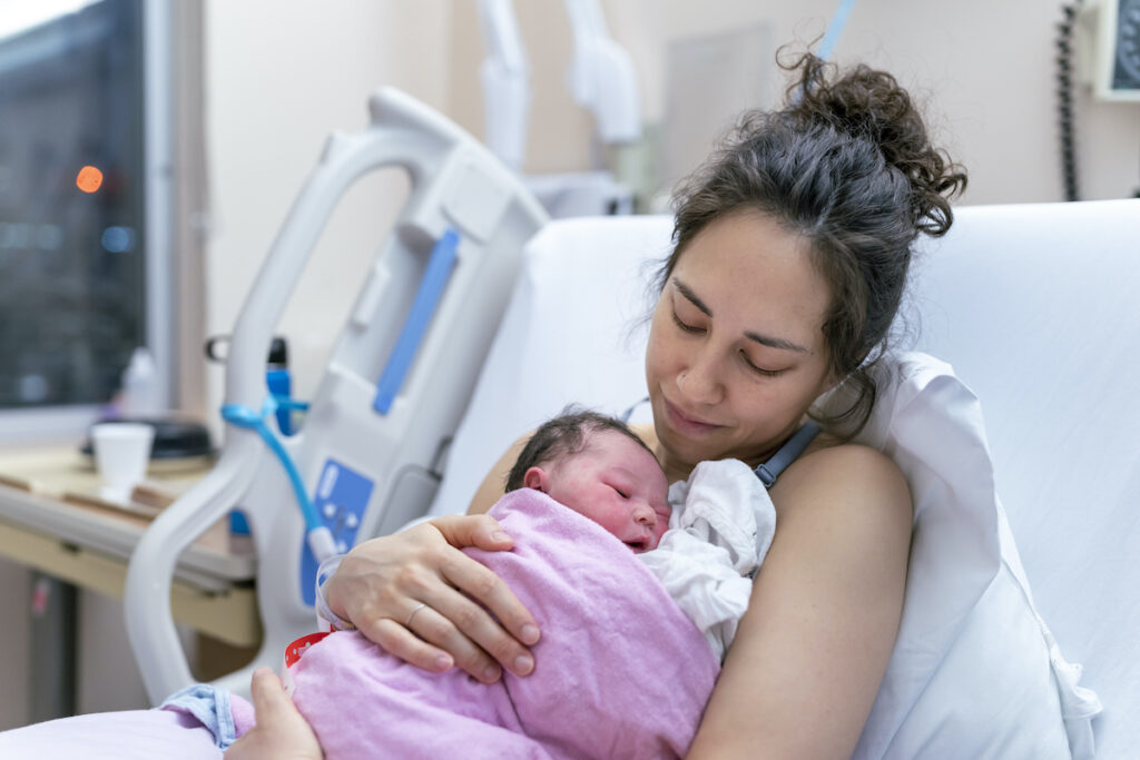 A new parent in a hospital beds holds a baby during skin to skin contact.
