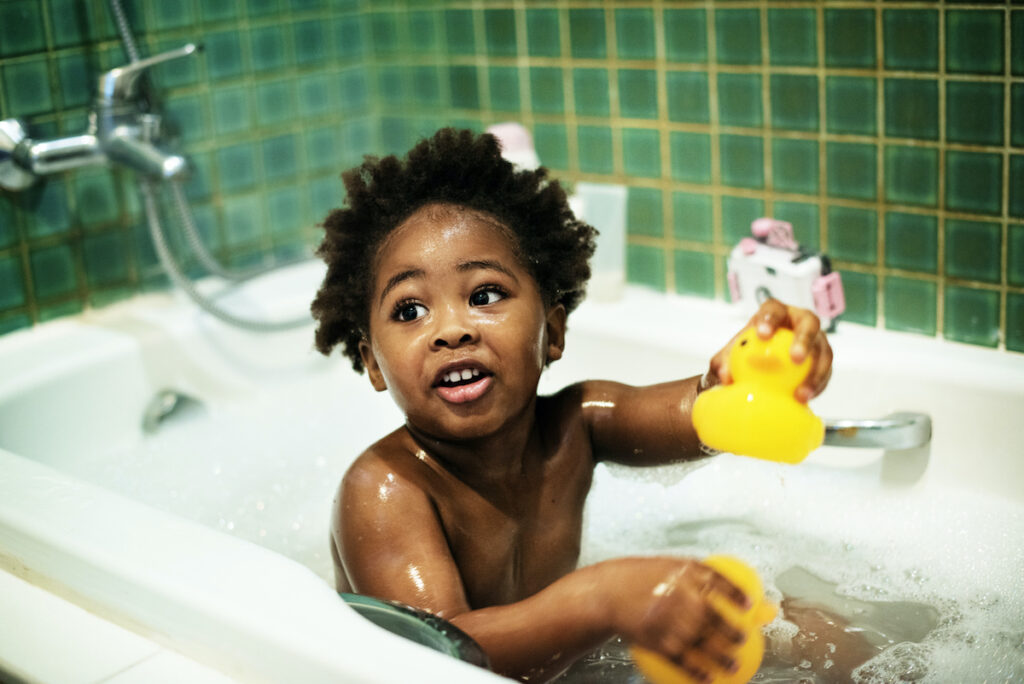 A baby sits in a tub full of bath water with a rubber ducky.