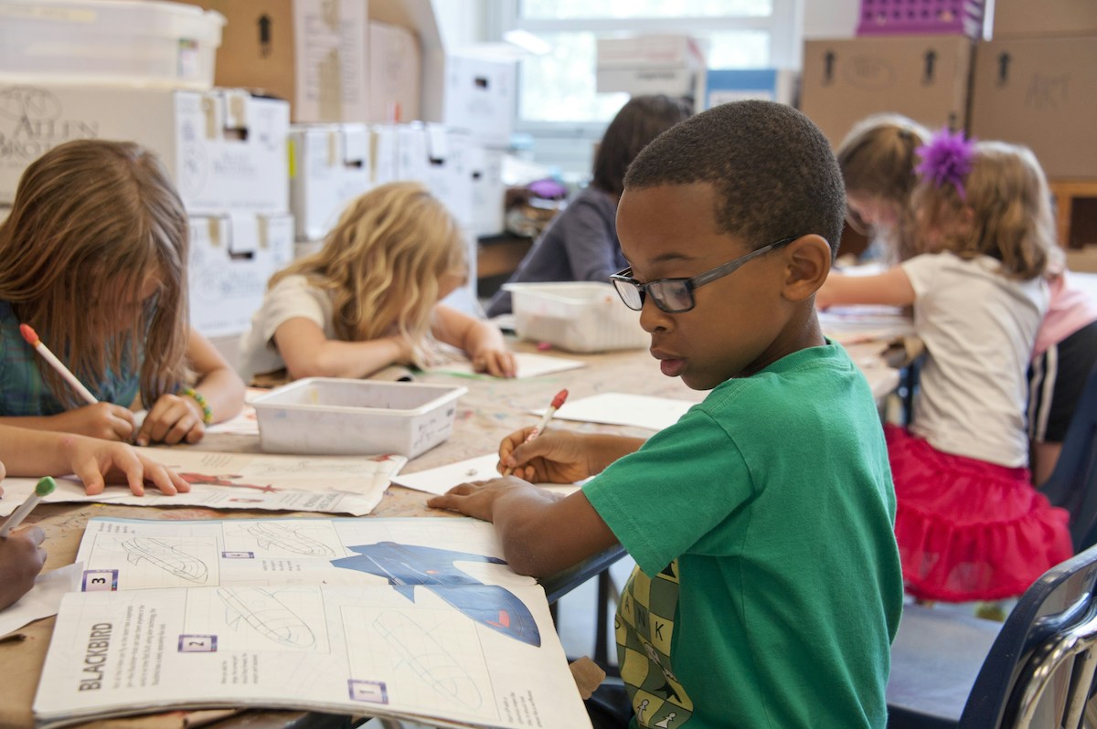 Kids draw and read at a table in a classroom.