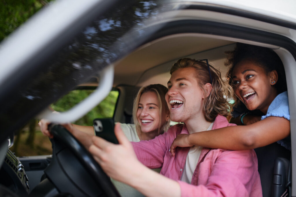 A group of young friends in a car, where the driver is laughing and holding a cell phone.