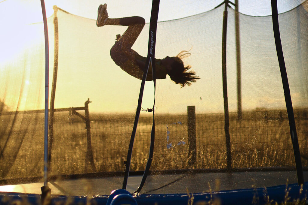 A big kid jumps on a trampoline outside at sunset.