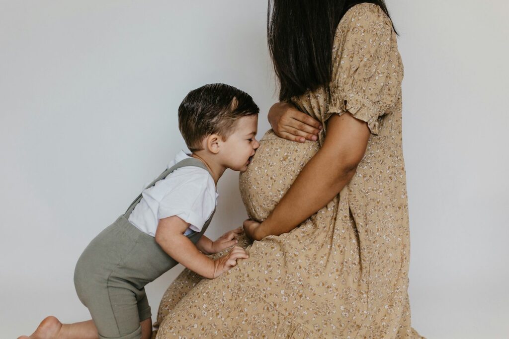 A toddler kisses the the pregnant belly of their parent.