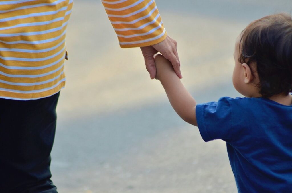 Parent in a yellow striped shirt holding the hand of a toddler.