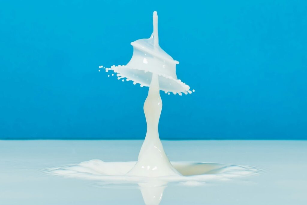A drop of milk splashes against a blue background to illustrate lab-produced breastmilk.