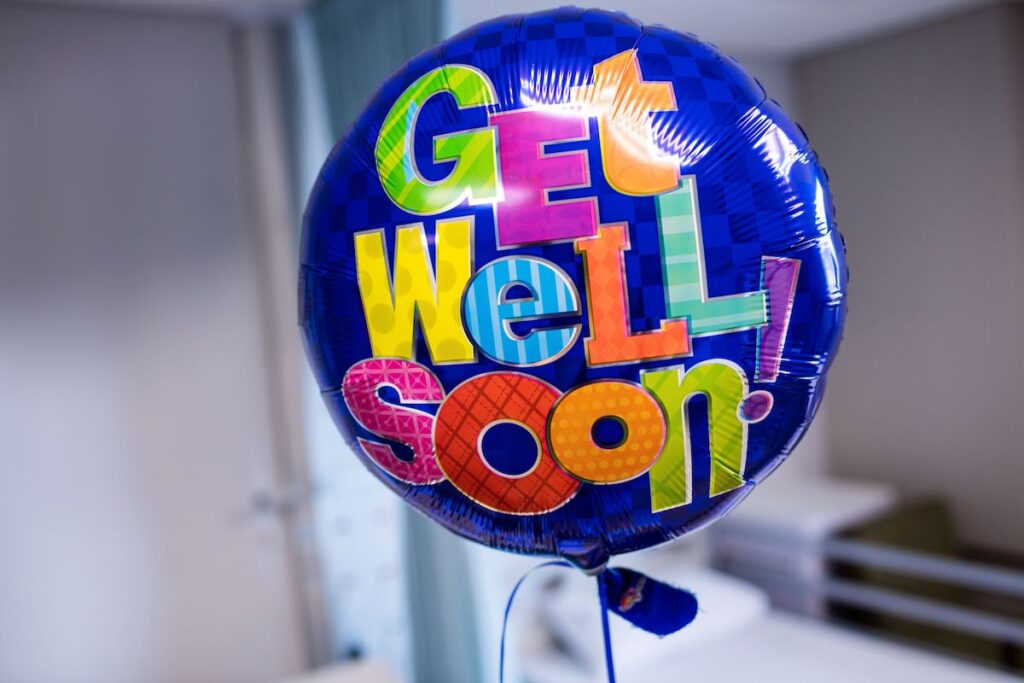 A "get well soon" balloon is seen against a hospital room.
