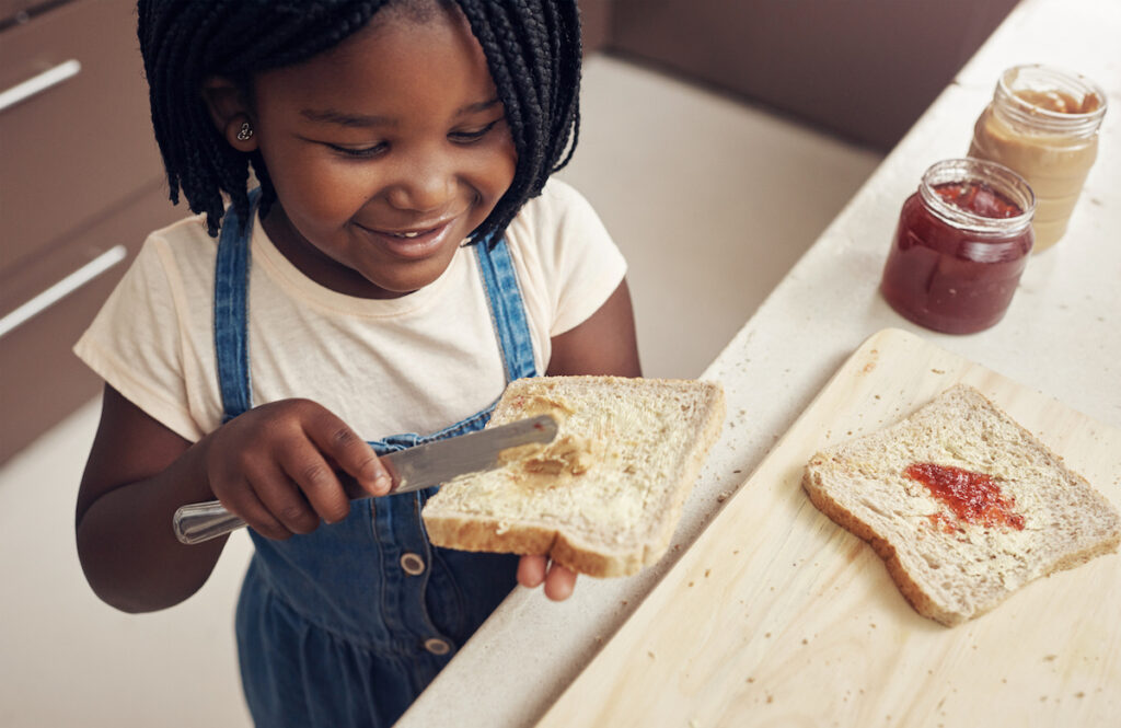 Child spreads peanut butter on bread.