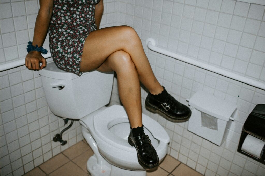 Person sitting on back of toilet with legs crossed
