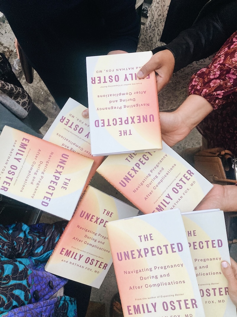 Many hands holding copies of "The Unexpected" by Emily Oster