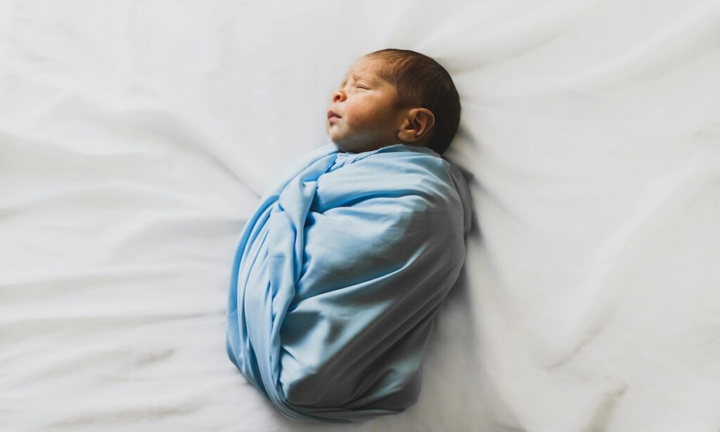 Swaddled infant asleep on back on white sheet