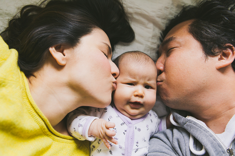 Two parents kiss a baby on either cheek.