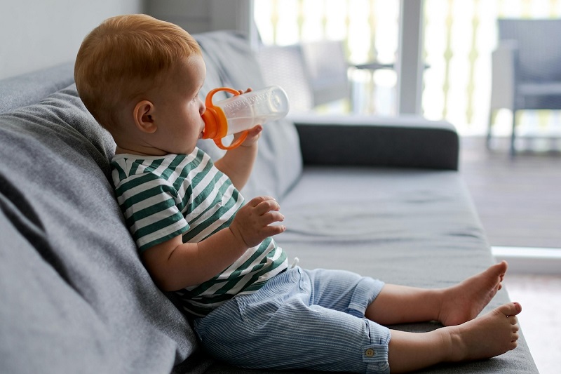 baby sitting on couch and drinking water through a feeder