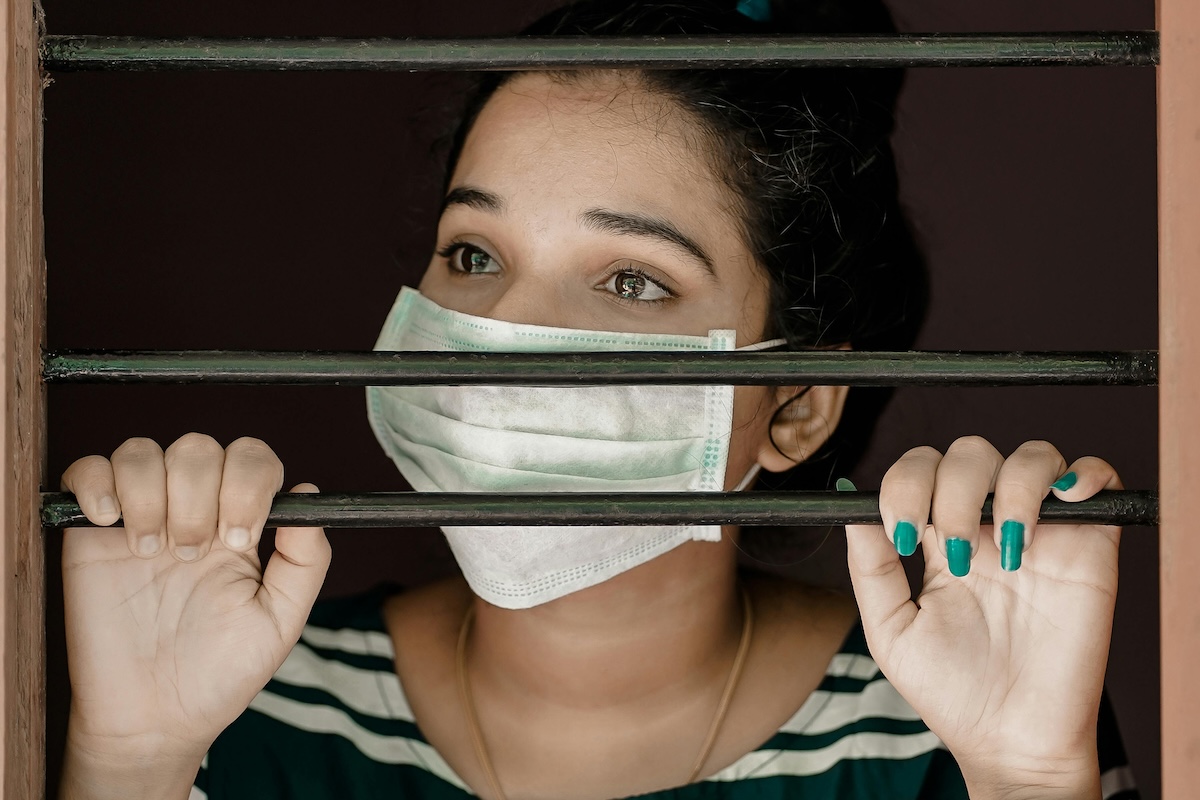 Person with a mask looking out of blinds