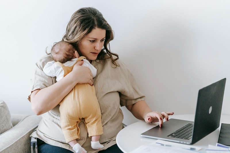 a parent holding a baby and using a laptop