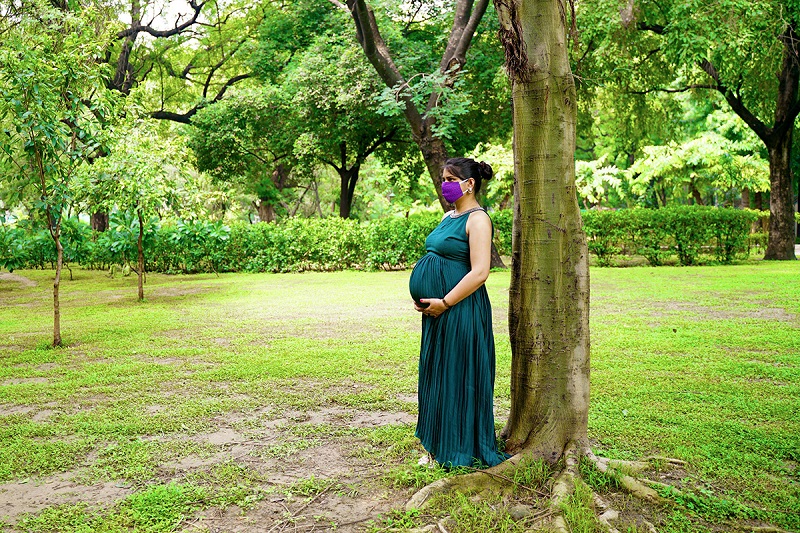 A pregnant adult person standing under a tree in a park