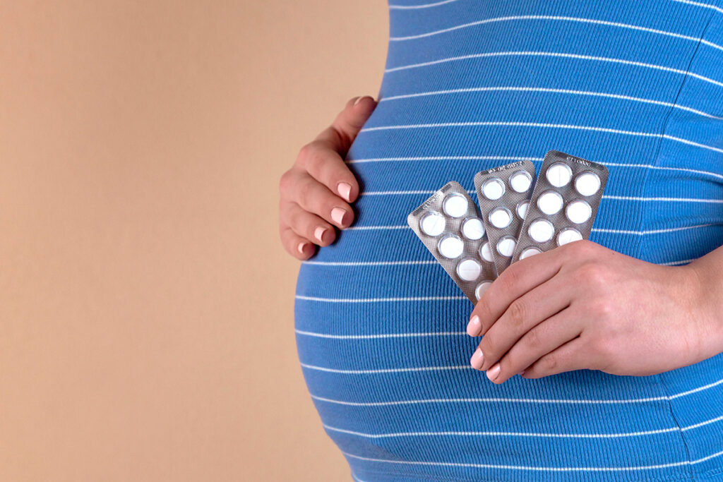 A pregnant person in blue shirt holding tablets