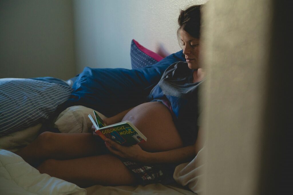 A pregnant person laying on bed and reading a book