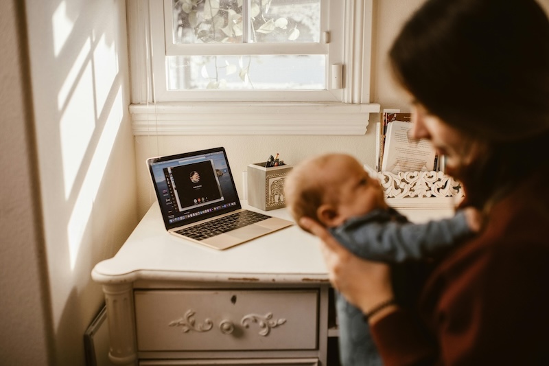 New parent holding a baby with a computer on desk in the background