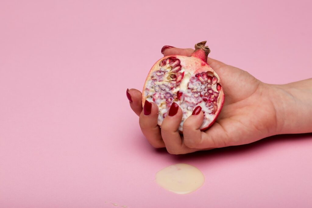 hand holding a half cut pomegranate with a pink background