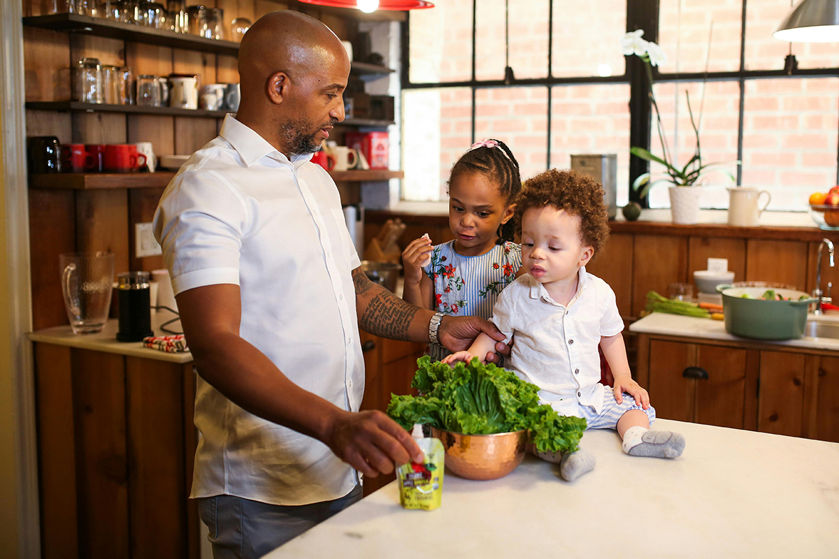 a person with two babies and having vegetables on the table