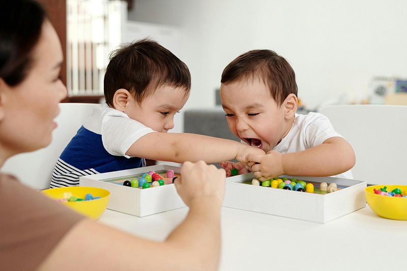 Kids playing with legos and one is trying to bit on the hand of other