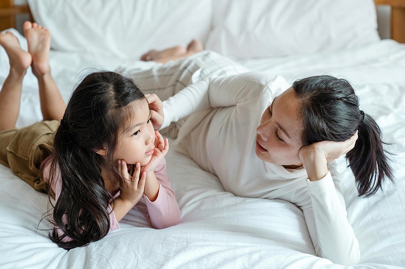 an adult and a kid laying on bed and talking