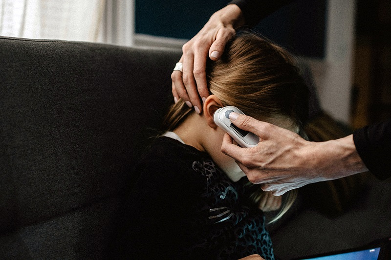 an adult checking fever of a child using a device near the ear