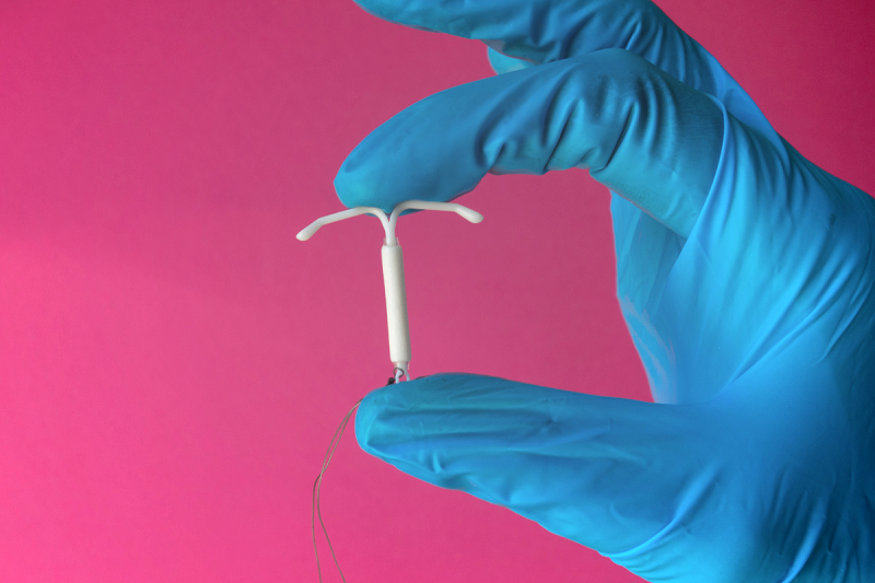 close up of a blue gloves hand holding an IUD device