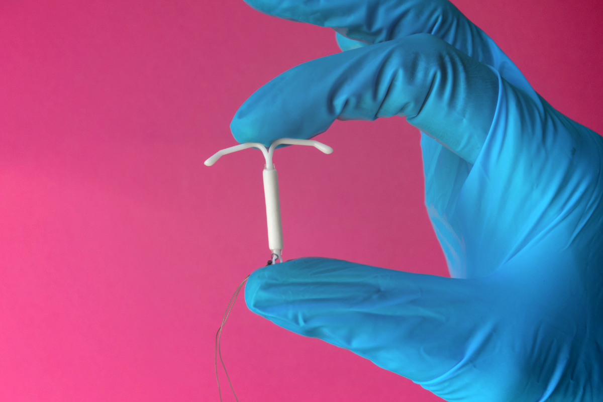 close up of a blue gloves hand holding an IUD device