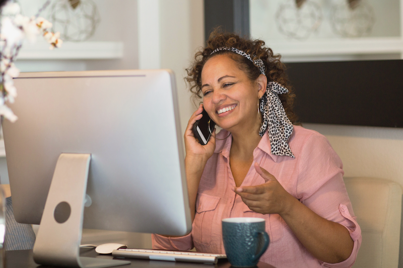 Person smiling talking on phone in front of computer screen