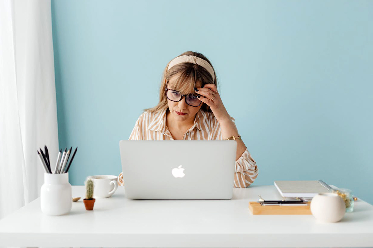 an adult sitting at a workplace using laptop and holding the head