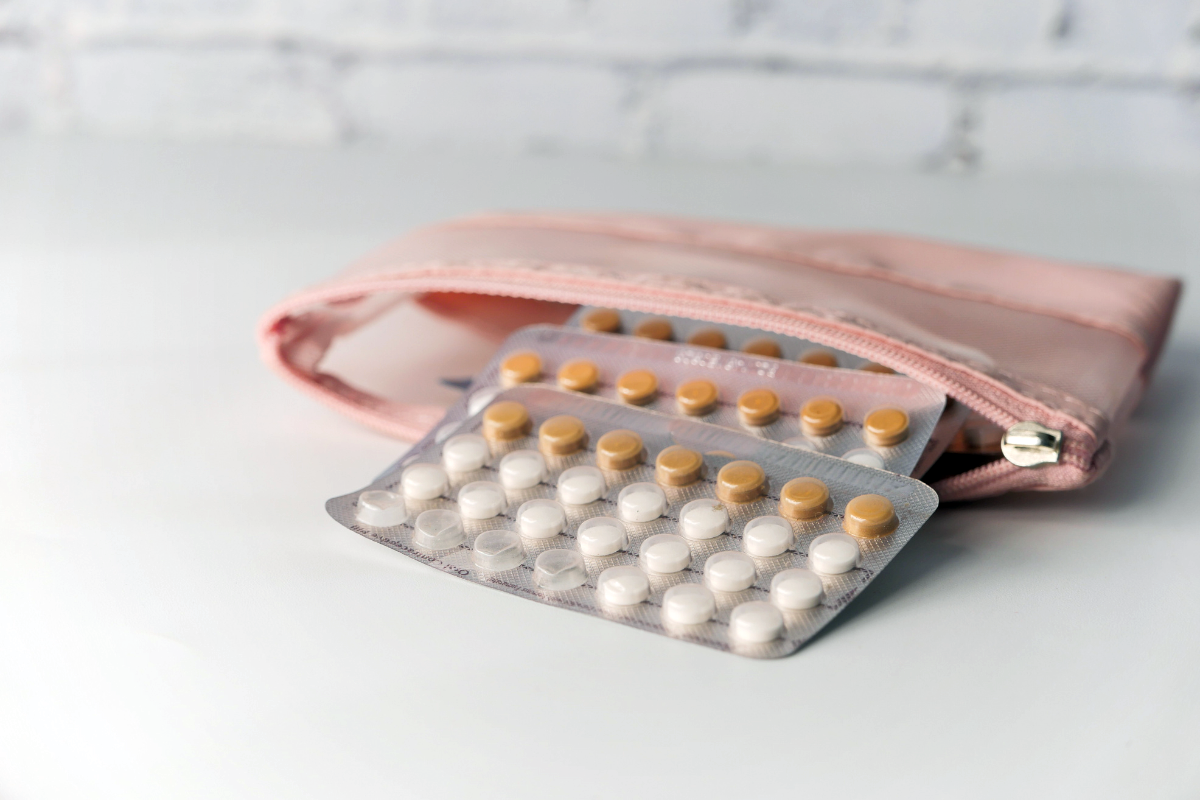 Packets of birth control pills spilling out of a pink pouch on a white counter.