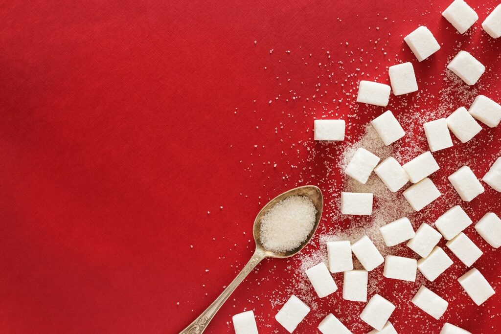 Sugar cubes and spoonful of sugar on red background